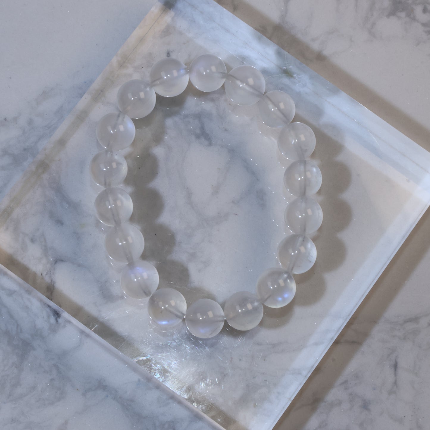 Top view of 11mm moonstone bracelet on clear acrylic block, showing soft milky translucence and blue sheen