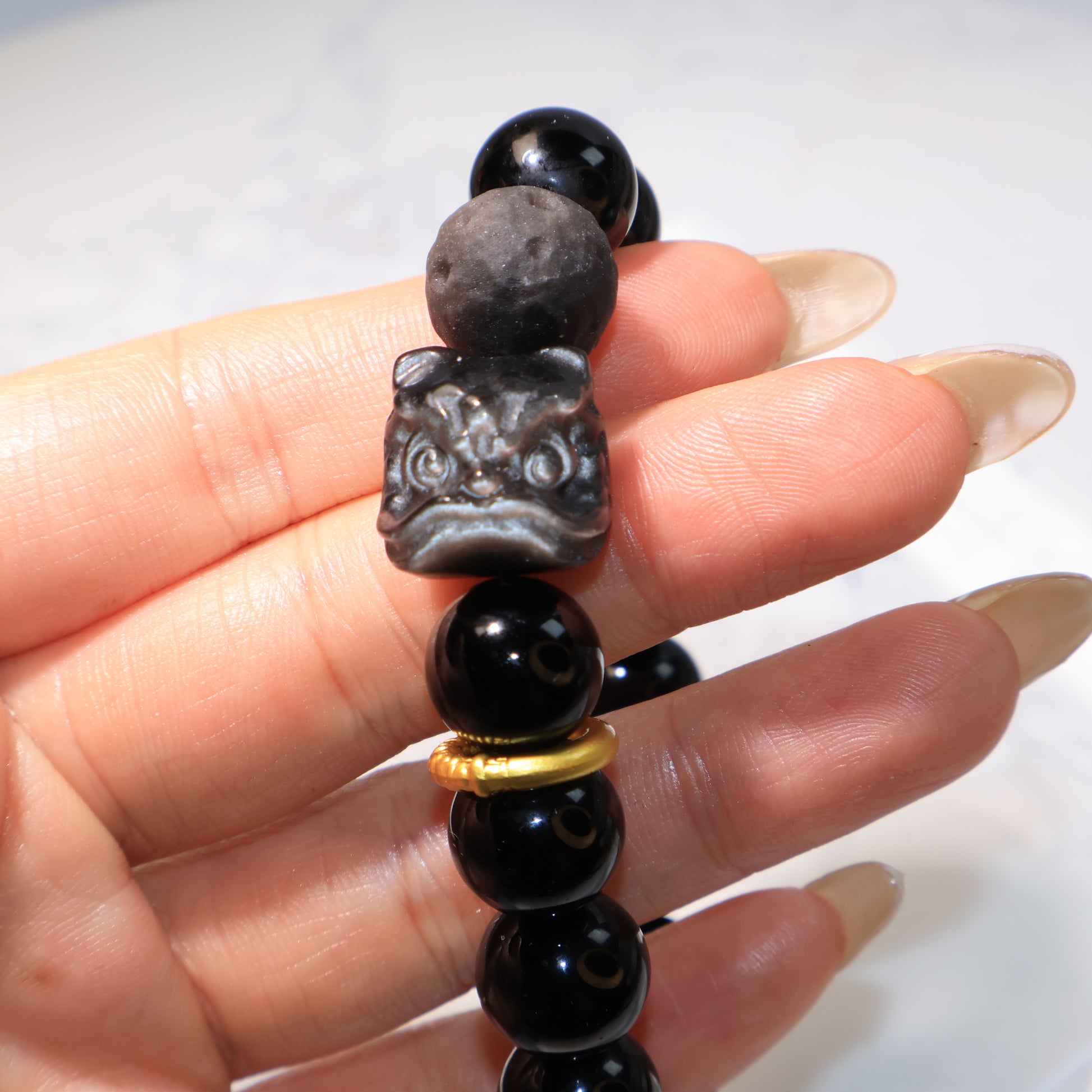 Close-up of Pixiu Lion carving, meteorite-inspired bead, and polished black obsidian – 手持展示黑曜石隕石醒獅手串特寫。