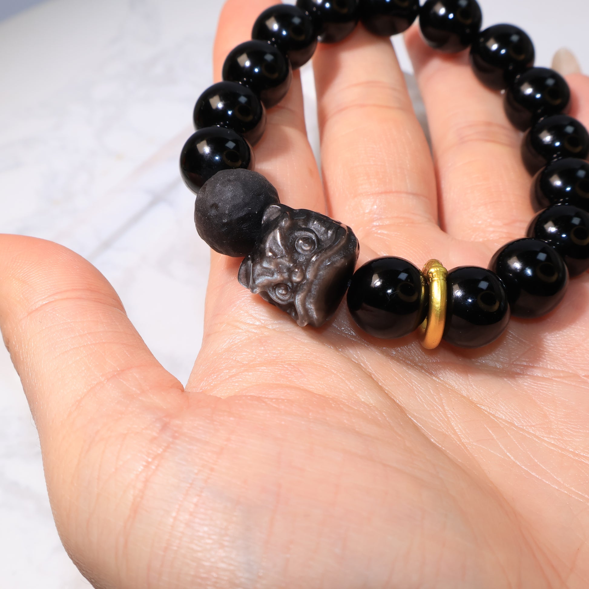 Bracelet resting on hand, highlighting Pixiu Lion bead and golden ring – 黑曜石隕石醒獅手串於掌心展示。