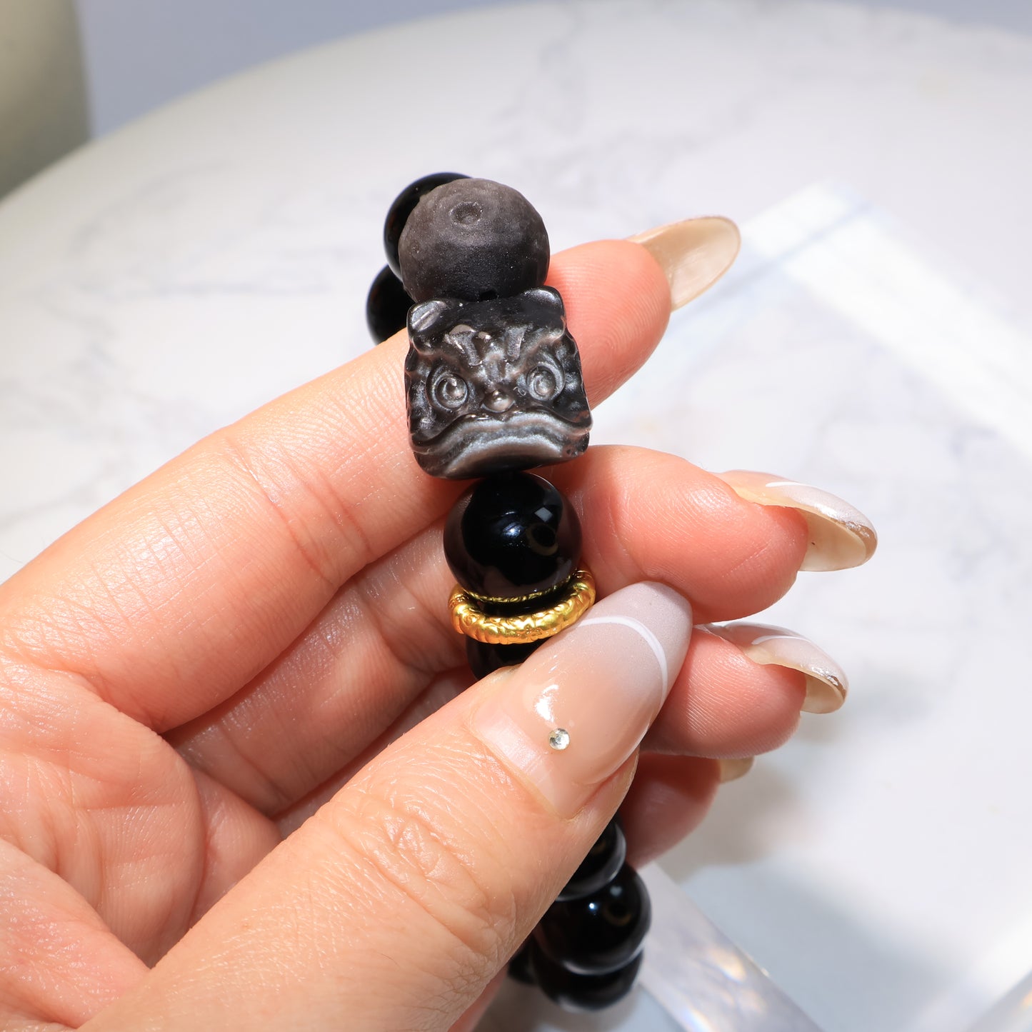 Obsidian bracelet angled view, showing the carved Pixiu Lion and golden accent – 黑曜石手串斜角展示，醒獅雕刻與金色配件清晰。