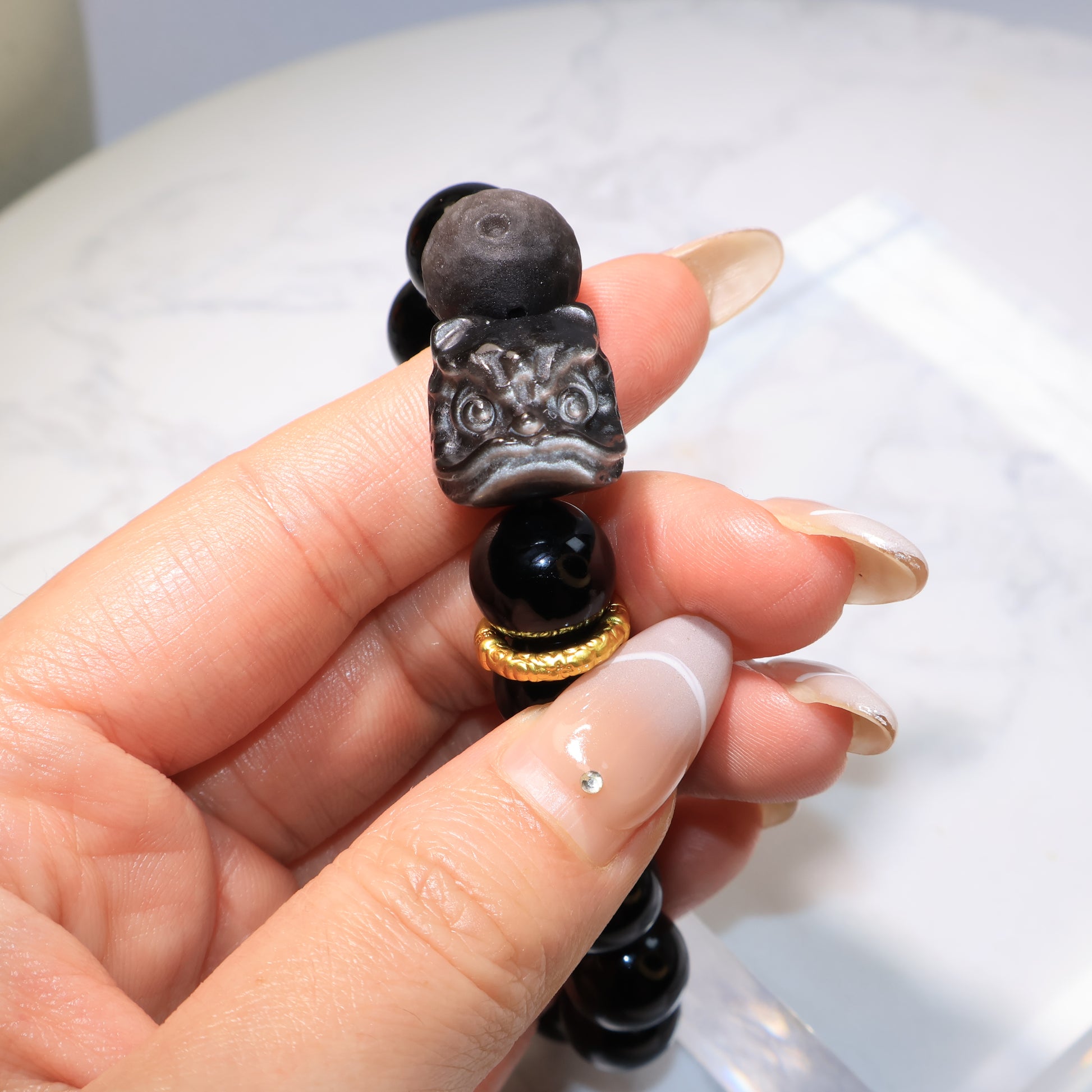 Obsidian bracelet angled view, showing the carved Pixiu Lion and golden accent – 黑曜石手串斜角展示，醒獅雕刻與金色配件清晰。