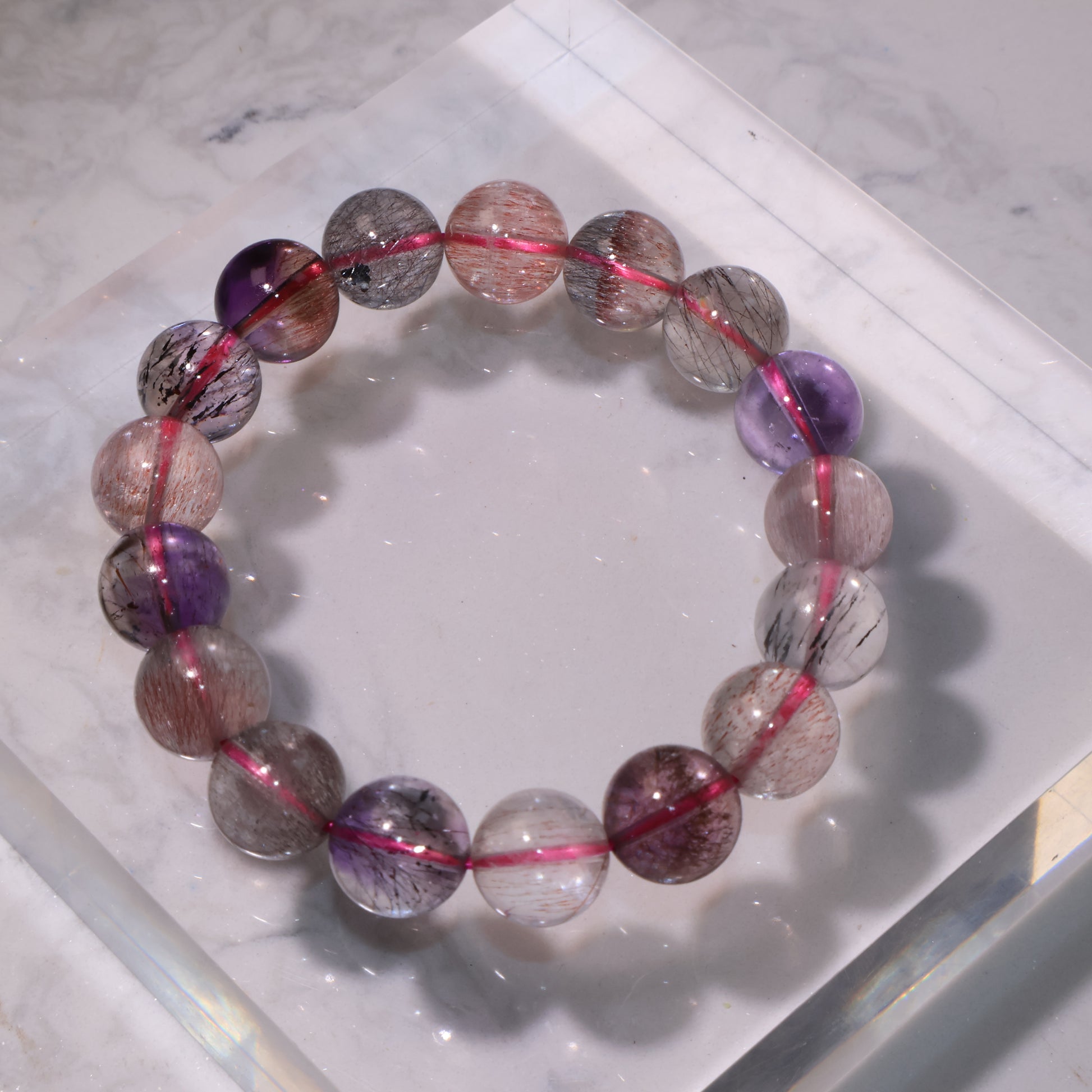 Super Seven bracelet on clear display stand, showing light yet transparent beads｜透明展示座上的超七手串，顏色淡雅但晶體透亮
