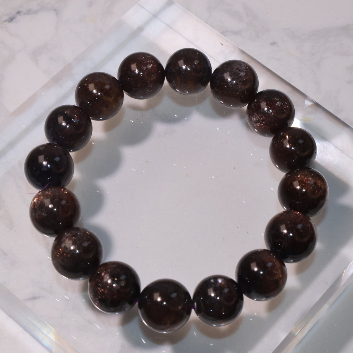 Eudialyte bracelet on clear display stand, showing deep reddish-brown tones｜透明底座上的血滴堇青手串，展現深紅褐色晶體