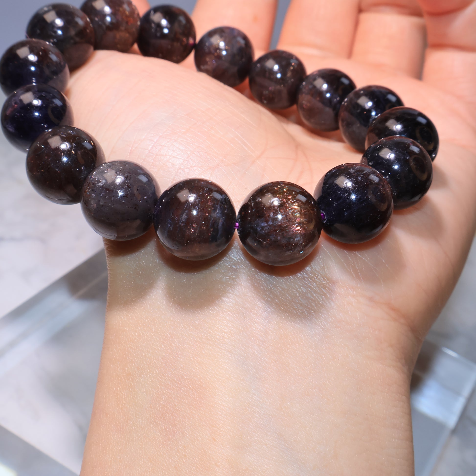 Close-up on wrist showing glossy dark red shimmer｜佩戴於手腕，晶體光澤中透出紅色閃光