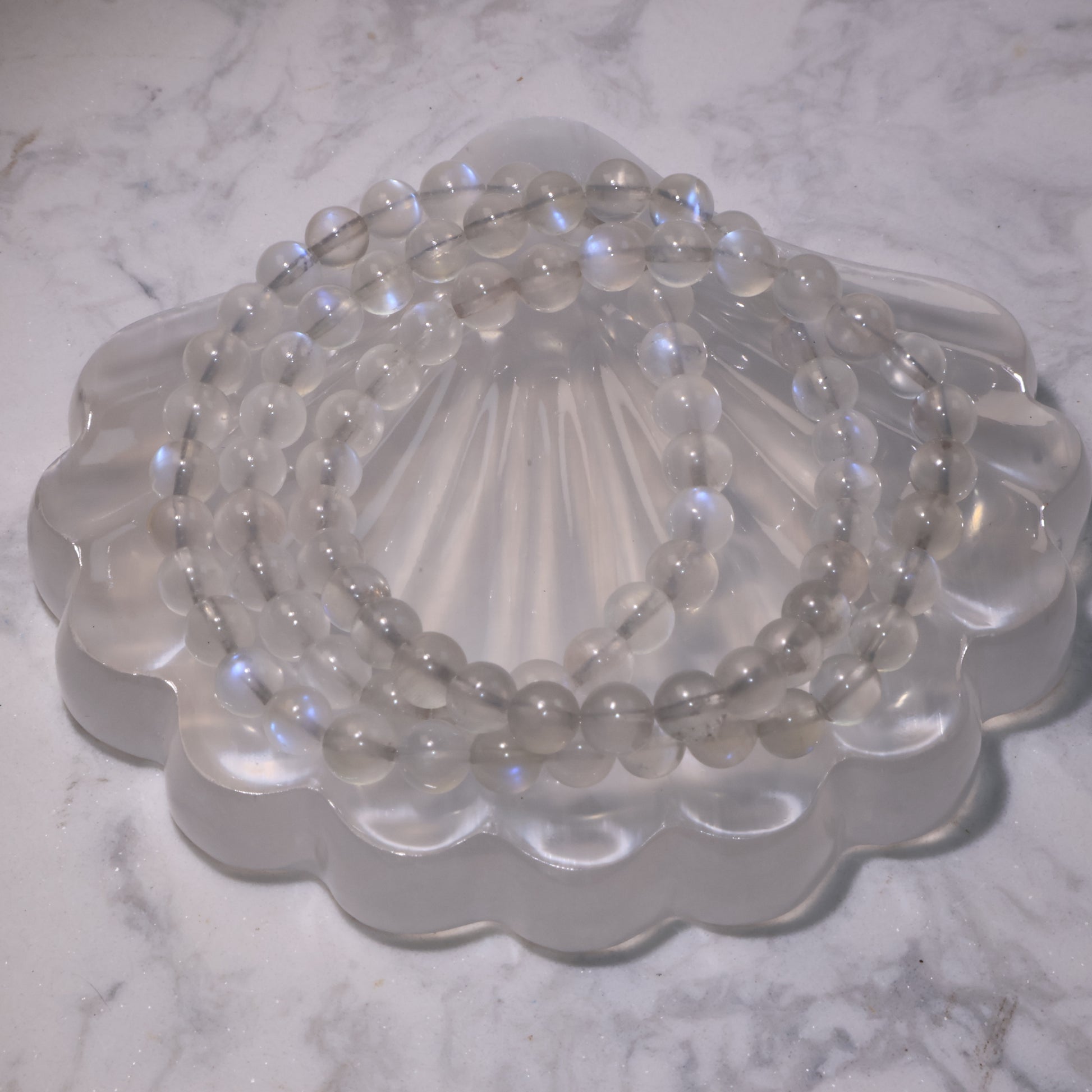 Close-up of a triple-wrap 6mm Moonstone bracelet on a shell-shaped crystal plate, showing its blue flashes.