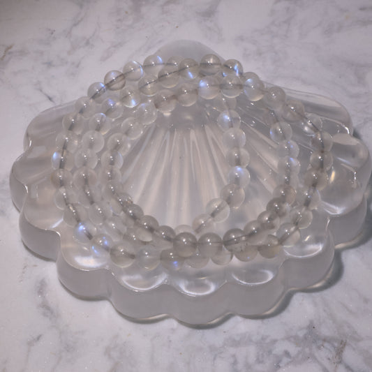 Close-up of a triple-wrap 6mm Moonstone bracelet on a shell-shaped crystal plate, showing its blue flashes.