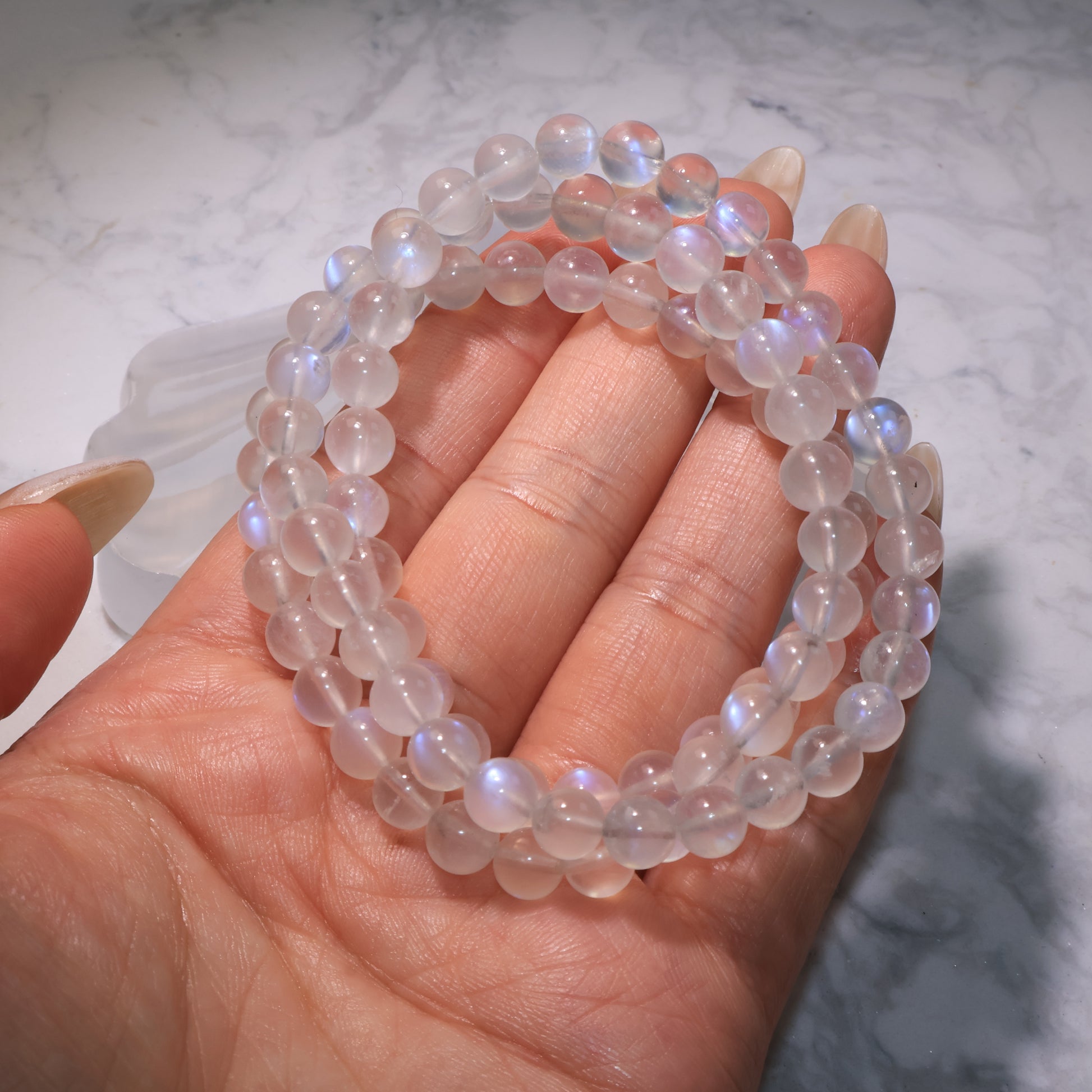 Moonstone bracelet with glowing blue sheen displayed on hand, highlighting its translucent beauty.