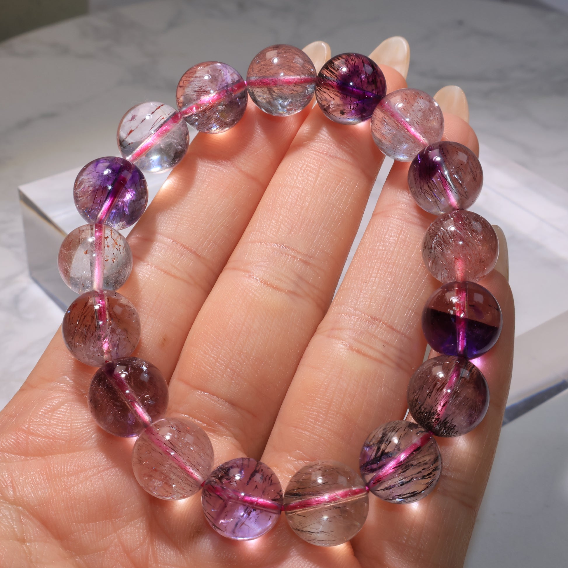Close-up of the Super Seven bracelet held in hand, highlighting the clarity and mixed inclusions of each bead.