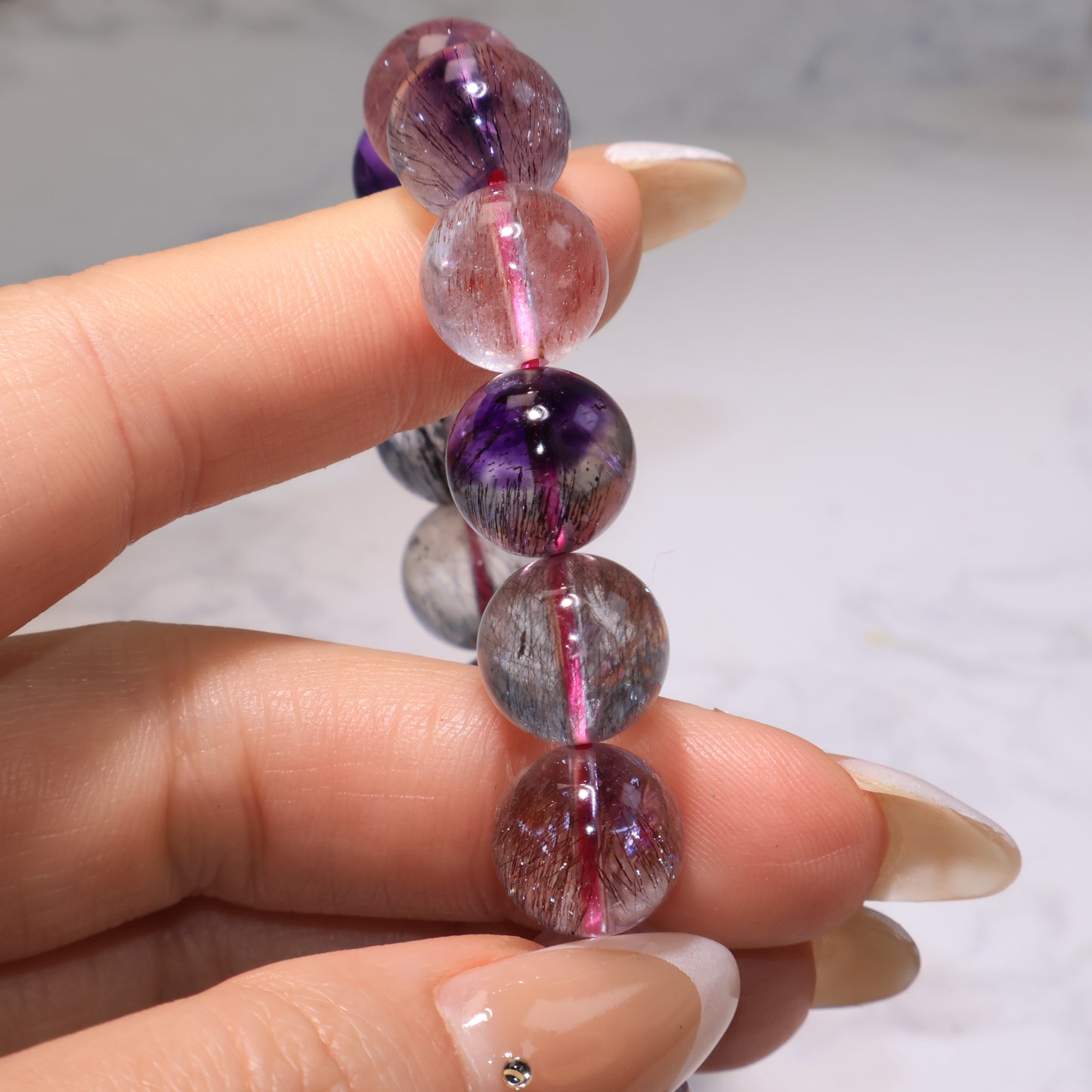 Fingers holding the bracelet, focusing on transparent beads with visible rutile inclusions.