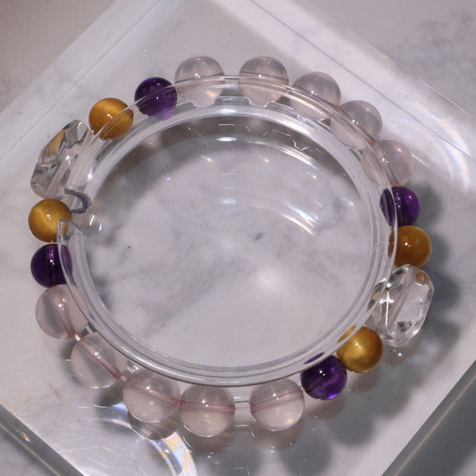 A crystal bracelet with Clear Quartz centerpiece, Rose Quartz, Amethyst, and Tiger’s Eye displayed on a clear stand.