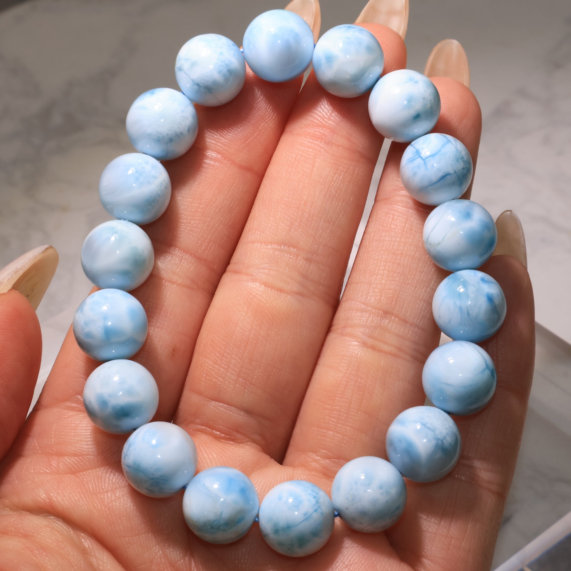 Hand holding a Larimar bracelet with polished blue and white beads, showing smooth surface details.