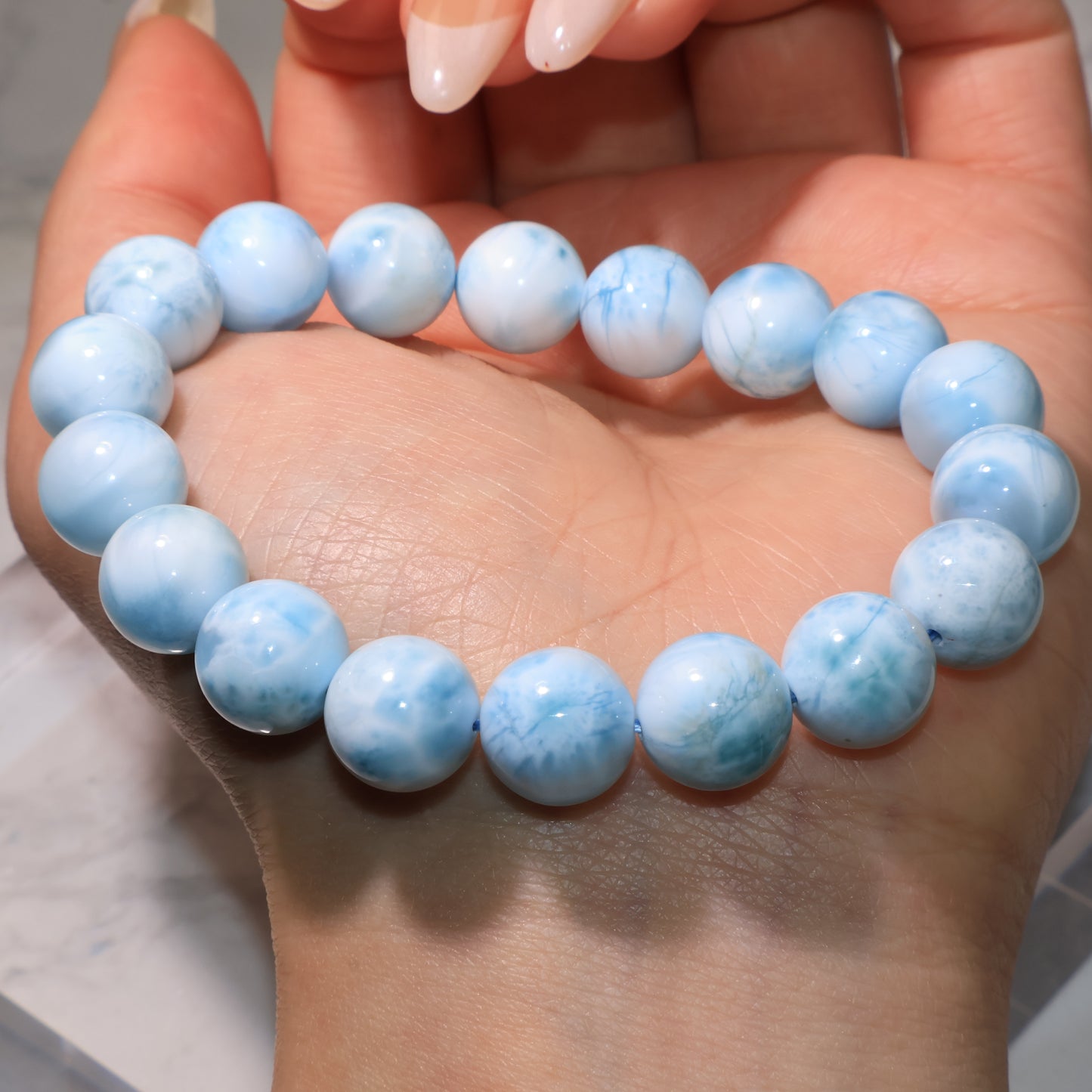 Larimar bracelet resting on the palm, round beads glowing under light.