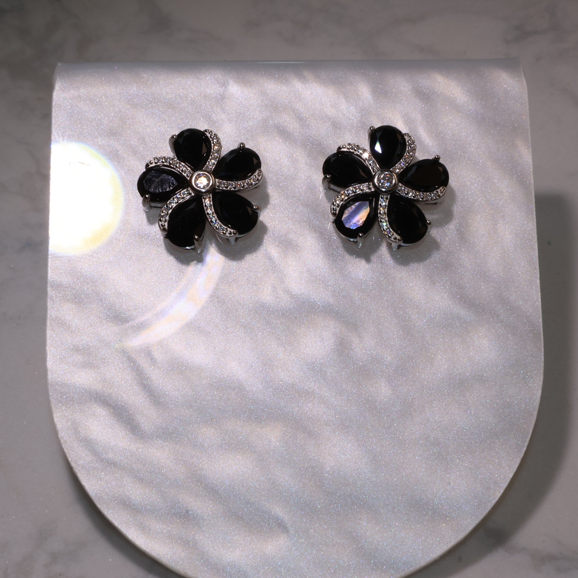 pair of black spinel flower earrings with zircon accents displayed on a pearly background.
