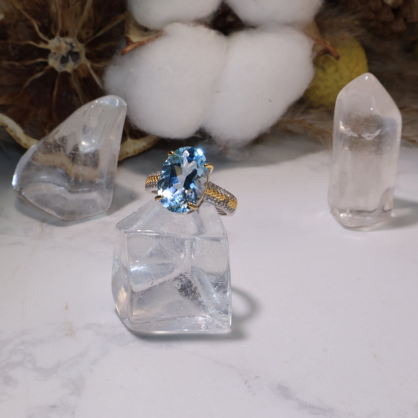 Front view of the ring with crystal props and cotton background, showing the brilliance and reflective facets of the topaz.