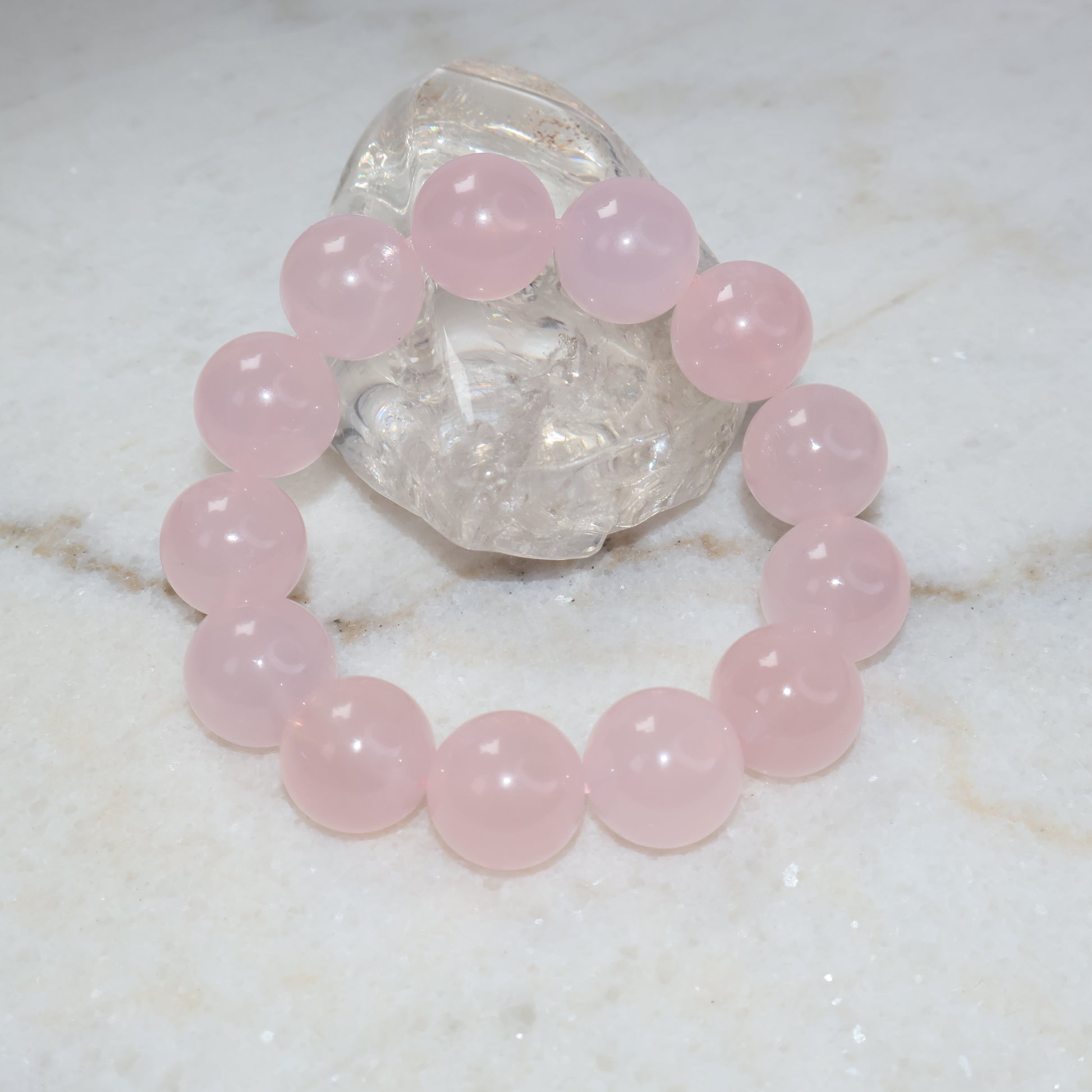 Natural 17mm rose quartz bracelet displayed with clear quartz crystal on marble background
