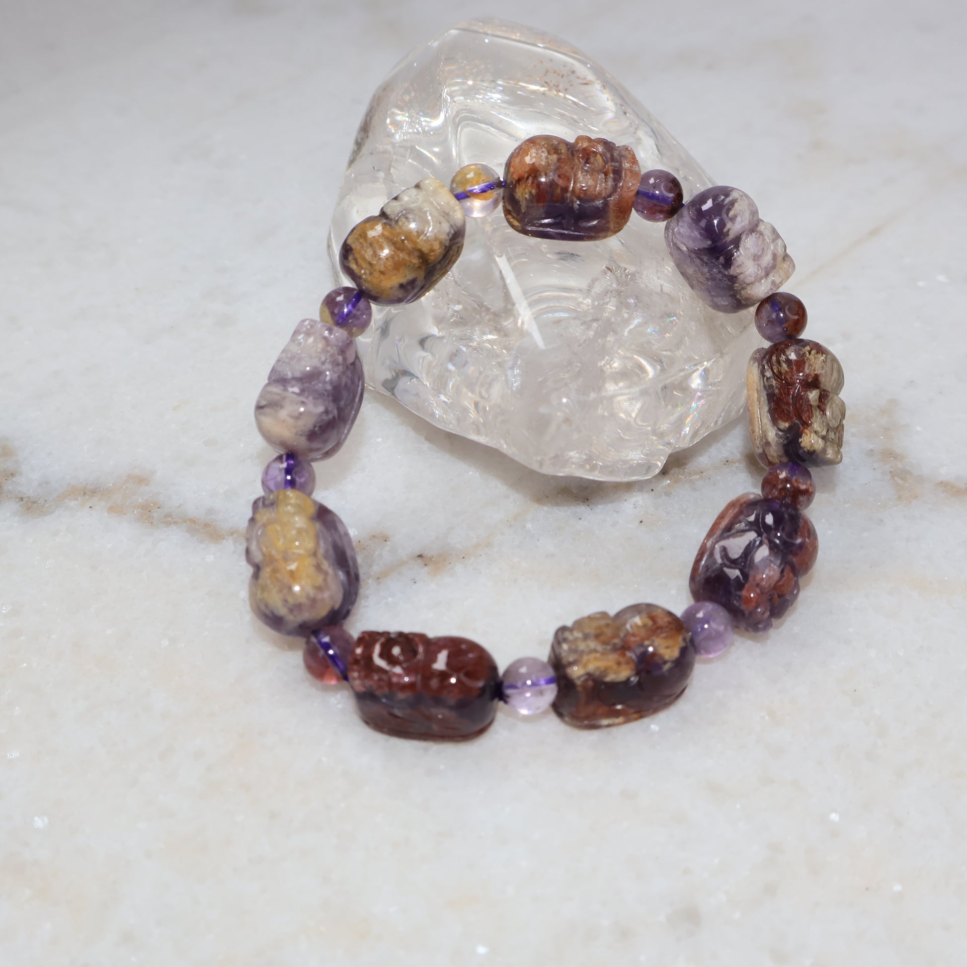 Purple phantom quartz Pixiu bracelet displayed with clear quartz crystal on marble background