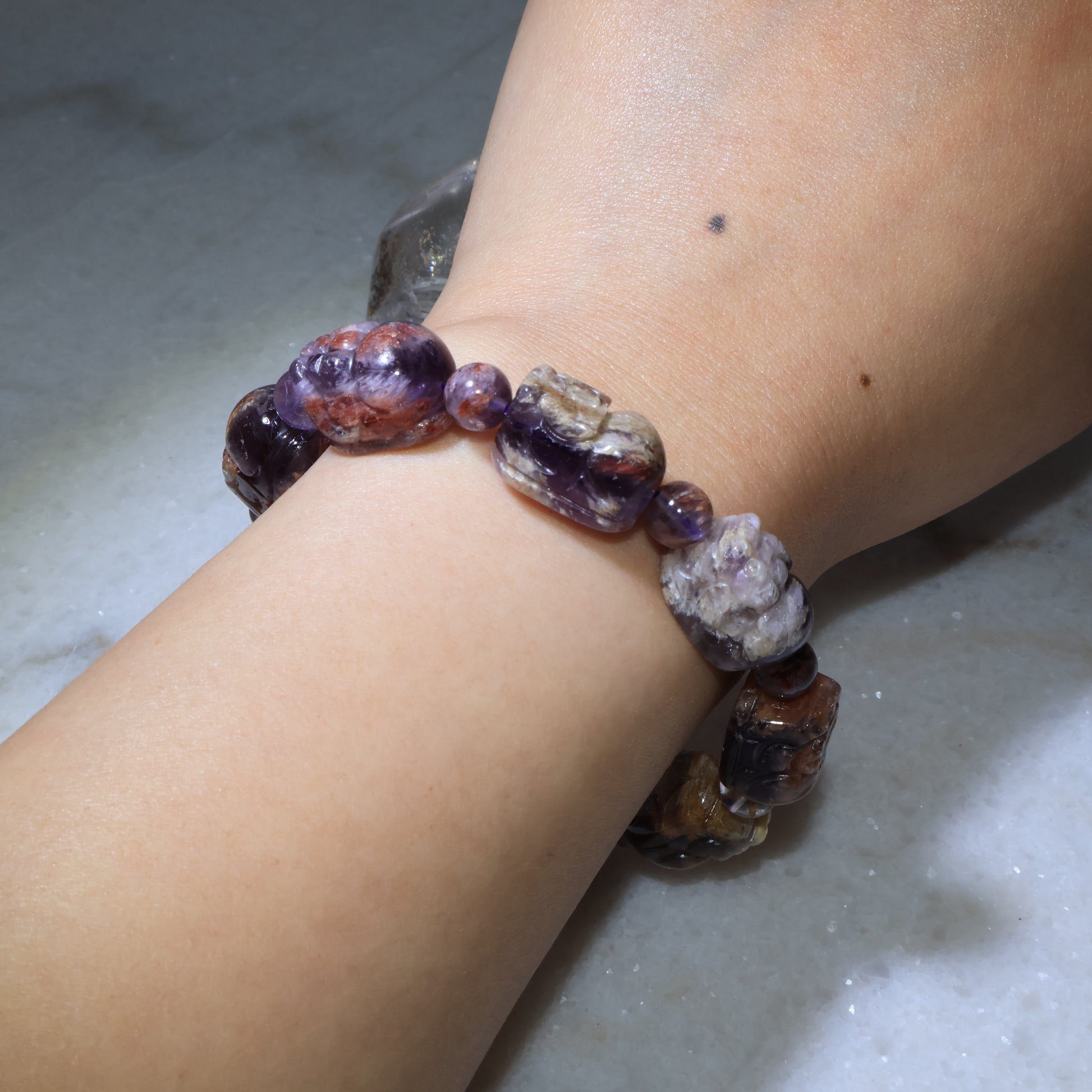 Close-up wrist shot of carved Pixiu crystal bracelet with purple and earthy tones