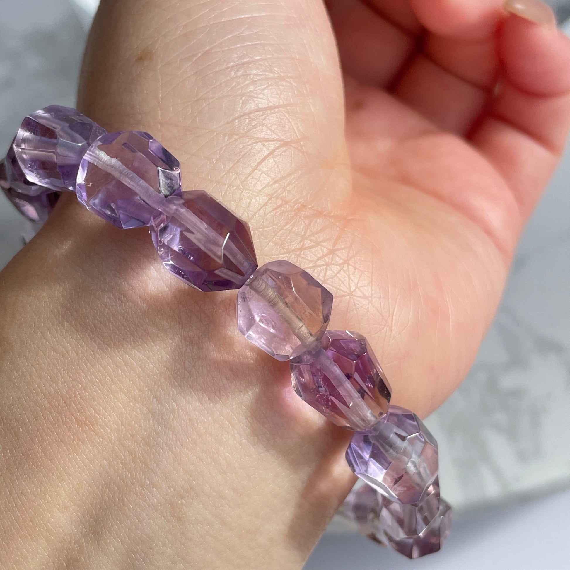 Close-up view of a raw-cut ametrine bracelet on the wrist, showing light purple and golden hues with high transparency and faceted surfaces under sunlight.