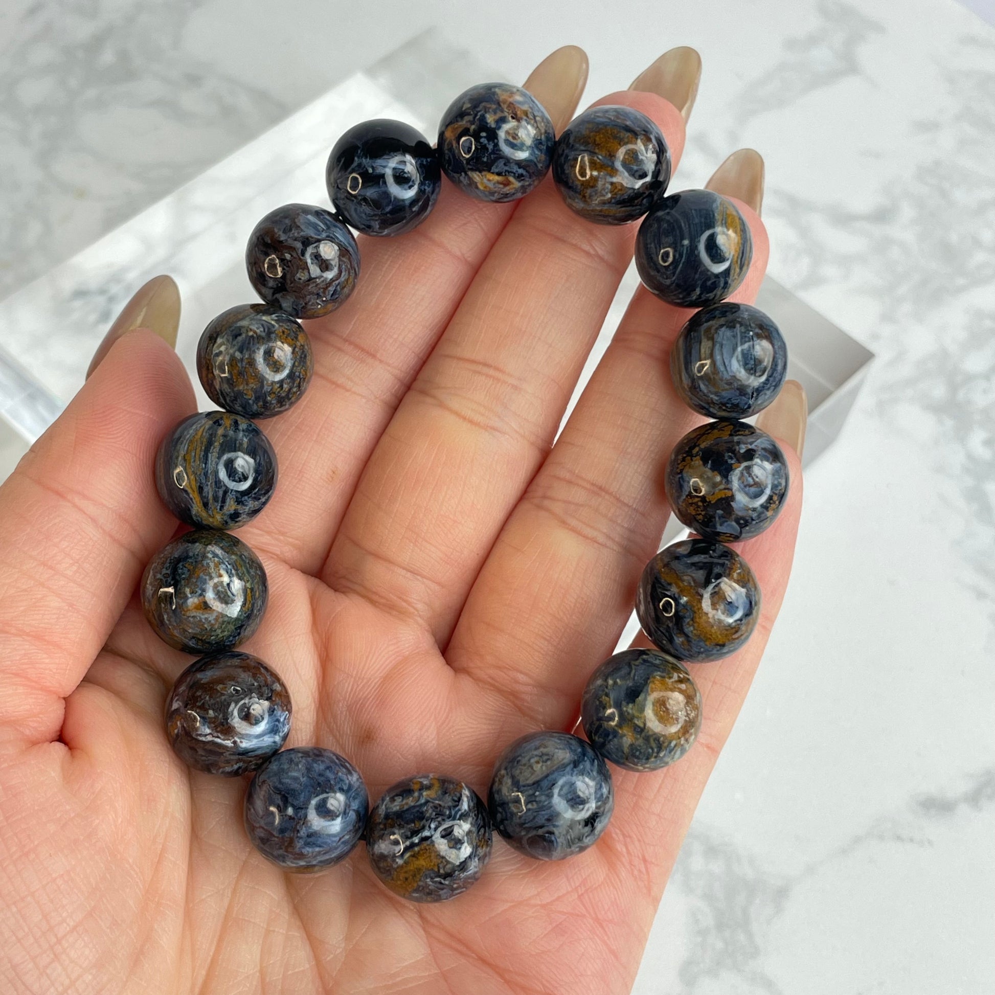 Power Core Pietersite bracelet close-up – 13mm polished beads in deep navy, golden brown, and silver streaks from Namibia, shown in hand for size and detail.
