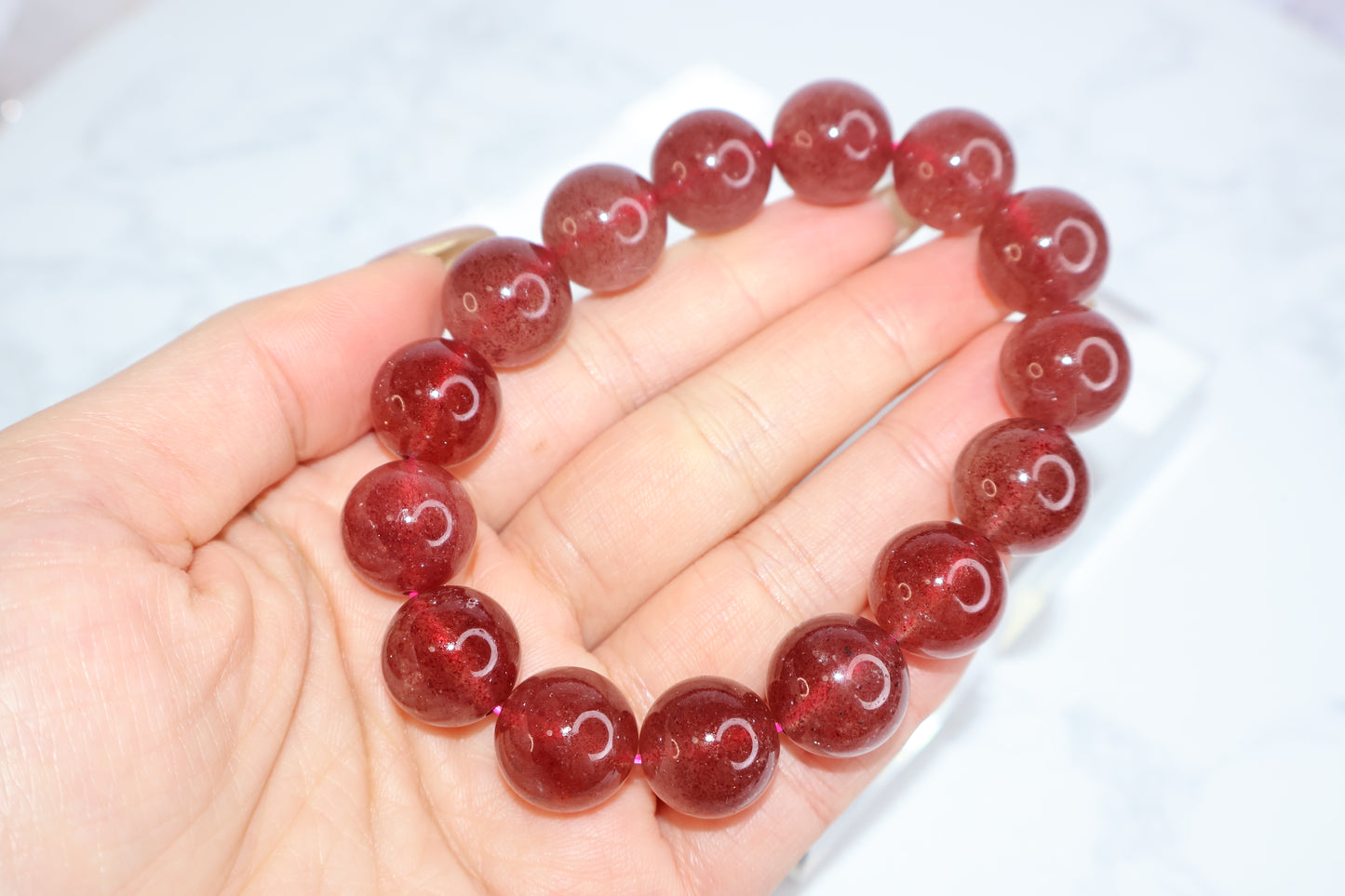 Hand holding a 14mm strawberry quartz crystal bracelet – deep red beads with glossy finish from Brazil, known for love energy and emotional healing