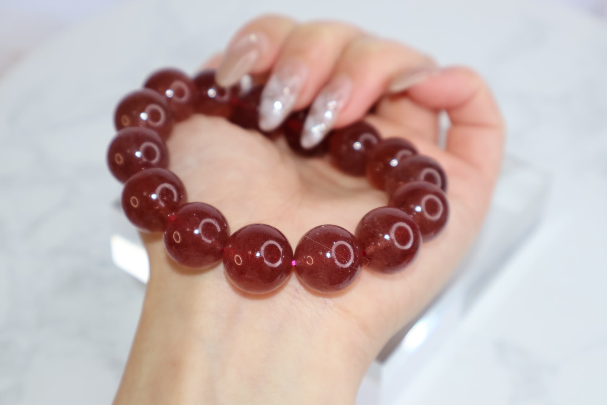 Strawberry quartz crystal bracelet 14mm held by hand – glossy deep red beads from Brazil, symbolizing love, beauty, and emotional healing.