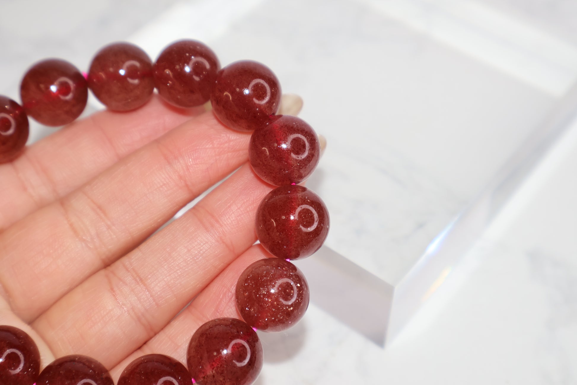 Close-up of 14mm strawberry quartz crystal bracelet – deep red glossy beads from Brazil shown on hand for love and emotional healing.