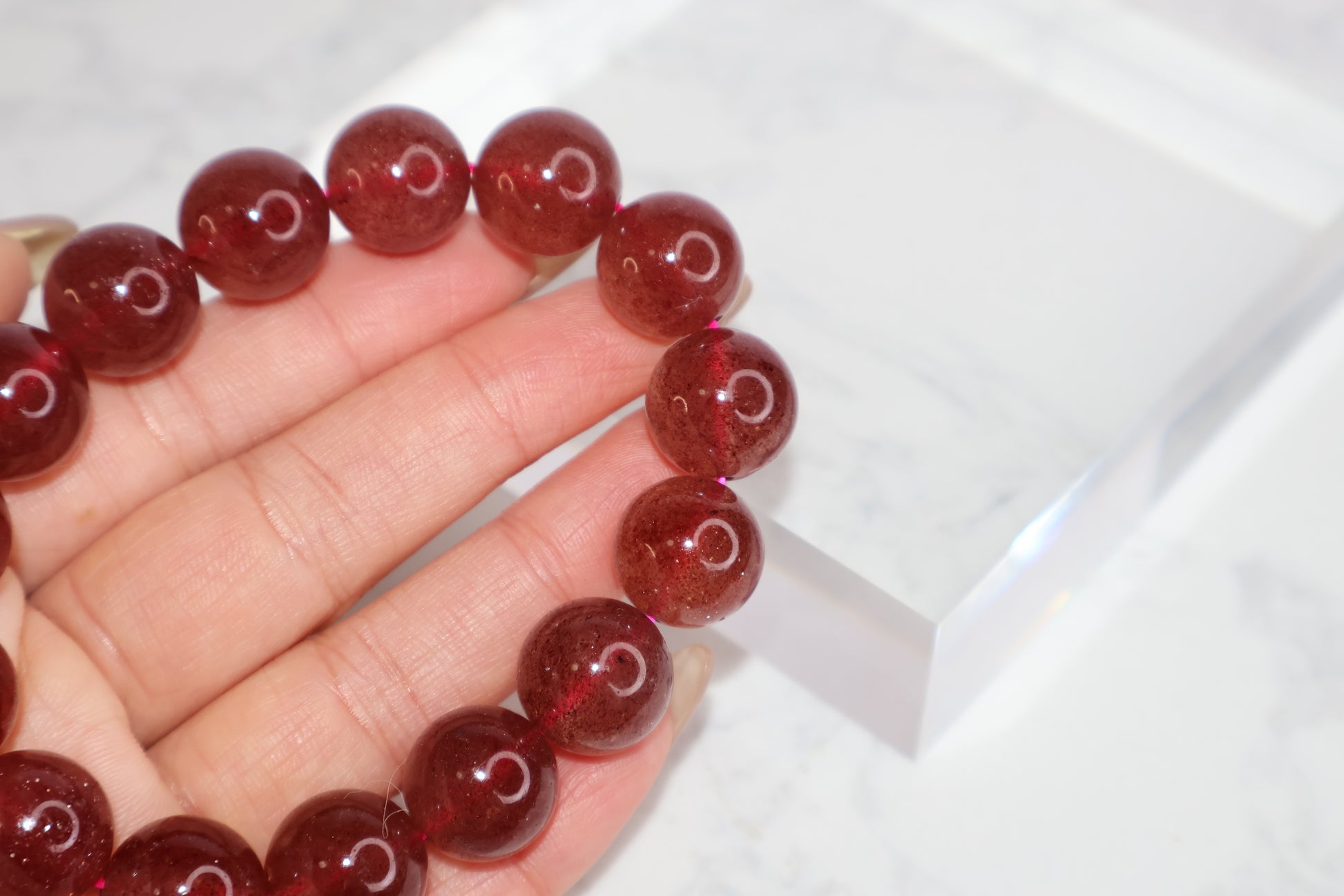 Close-up view of Heart Awakening 14mm strawberry quartz bracelet – deep red Brazilian beads with glossy surface shown in hand for love and emotional energy.