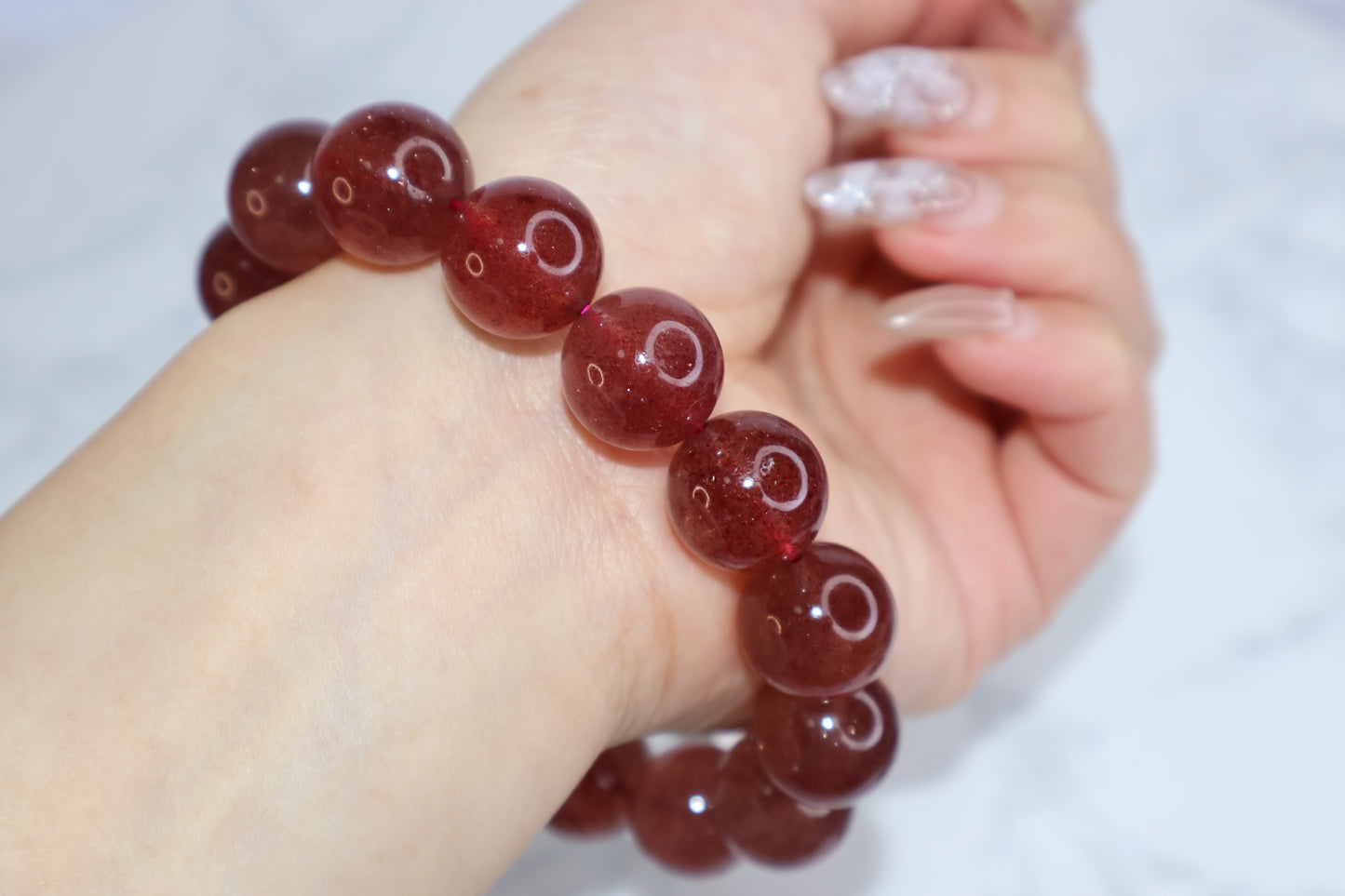 Heart Awakening 14mm strawberry quartz bracelet on wrist – Brazilian deep red crystal beads shown with natural light reflection, emphasizing bead clarity and wearability.