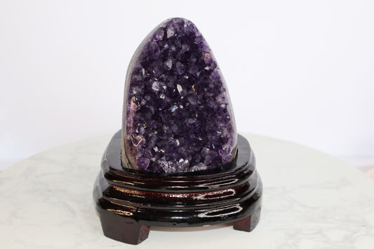 Front view of a deep purple amethyst geode standing on a dark polished wooden base, showcasing lustrous crystal points.