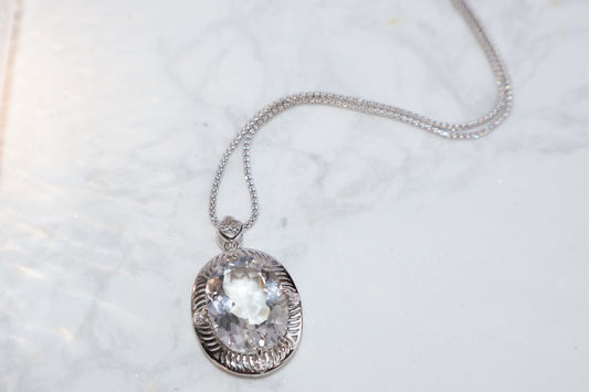 Clear quartz pendant on silver setting, oval cut, laid on marble surface
