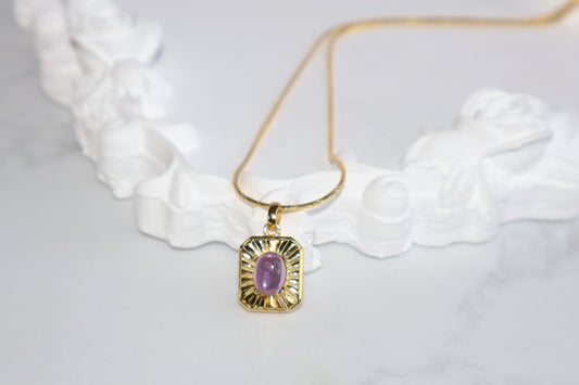 Amethyst cabochon pendant on golden chain, styled on marble background