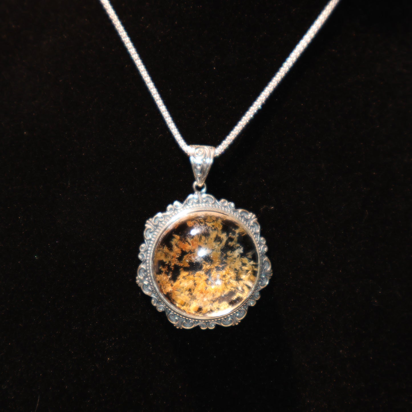 Dark background photo highlighting golden-black mineral inclusions and silver craftsmanship.
