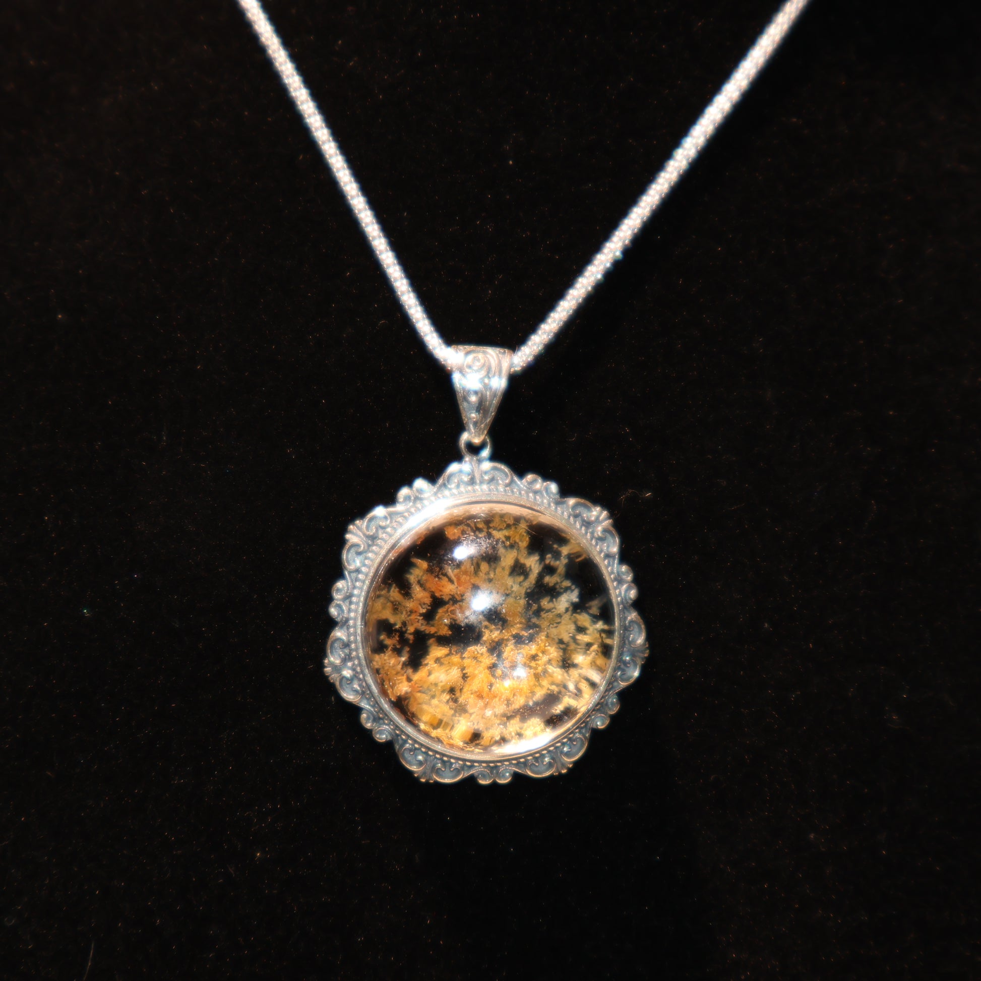 Dark background photo highlighting golden-black mineral inclusions and silver craftsmanship.