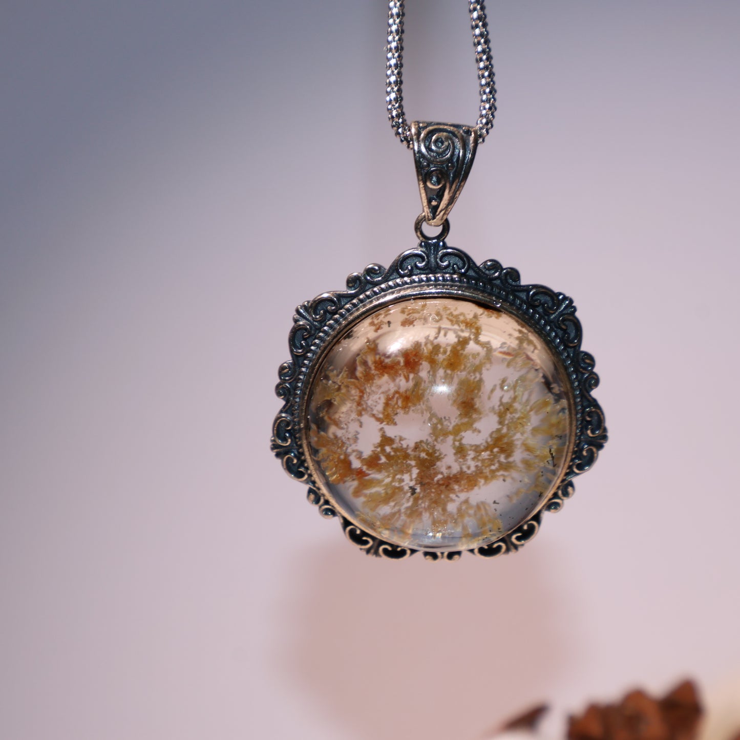 Pendant held in hand for scale, showing vivid inner landscape and silver detailing.