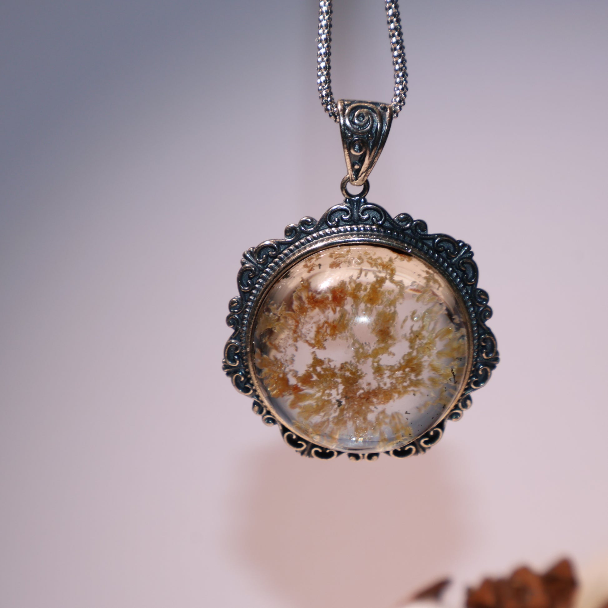Pendant held in hand for scale, showing vivid inner landscape and silver detailing.