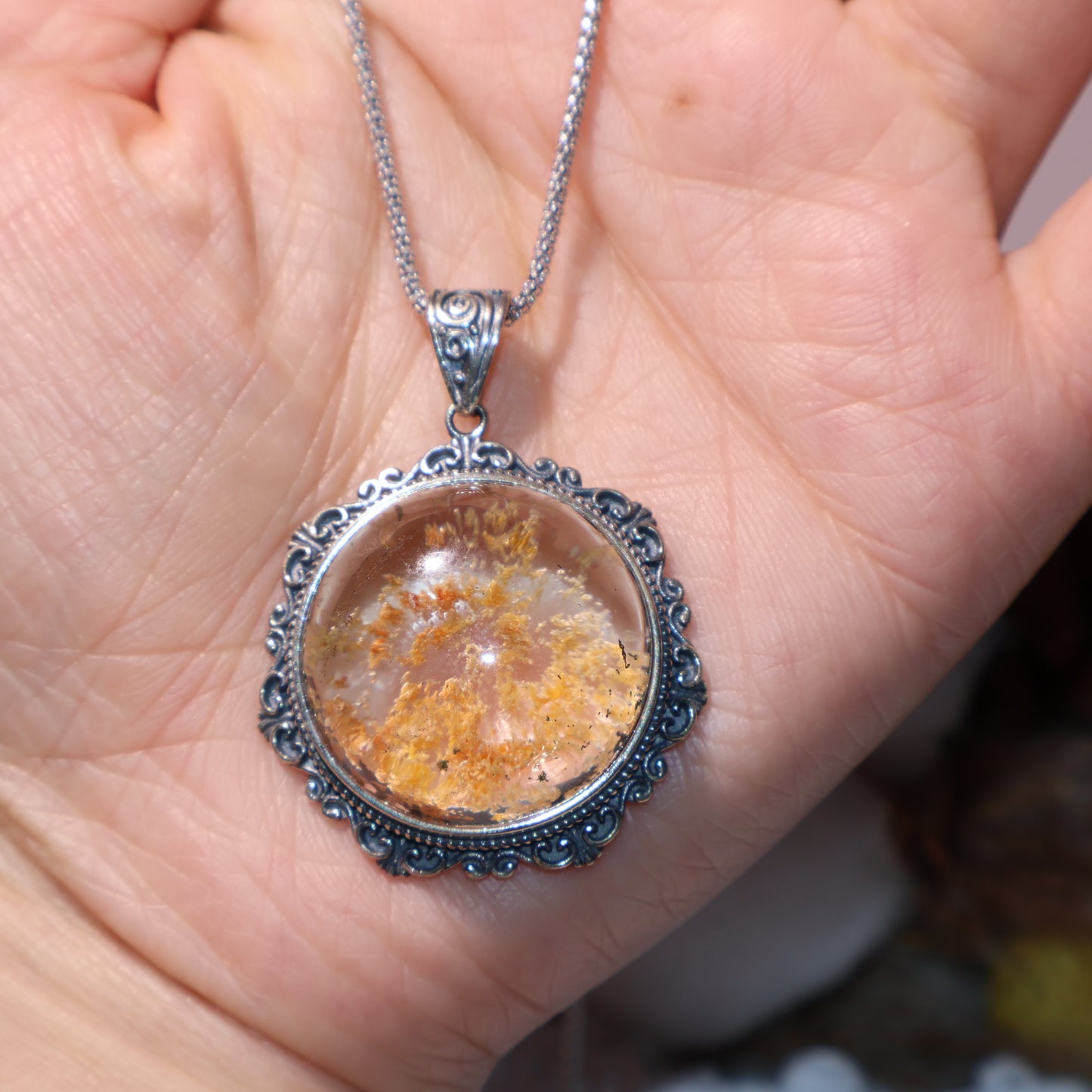 Pendant held in hand for scale, showing vivid inner landscape and silver detailing.