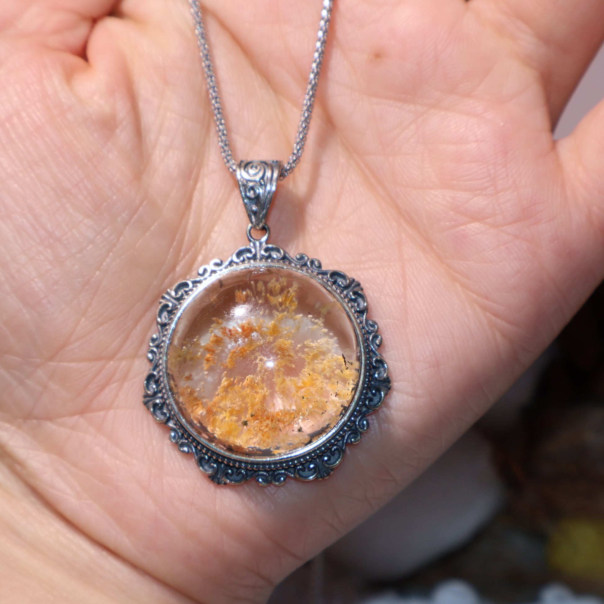 Pendant held in hand for scale, showing vivid inner landscape and silver detailing.