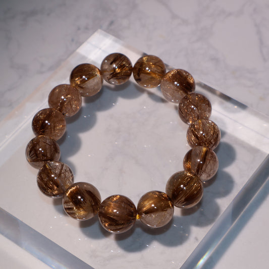 Flat lay of 13mm golden brown rutilated quartz bracelet on clear display block