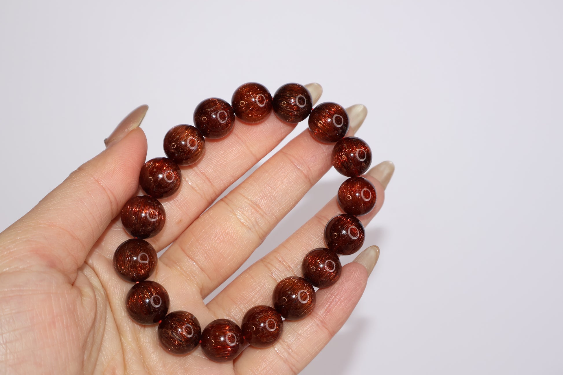 Red Rutilated Quartz bracelet with silky hair-like inclusions, shown in hand for scale and clarity, high-grade cat’s eye effect crystal beads for vitality and charm.