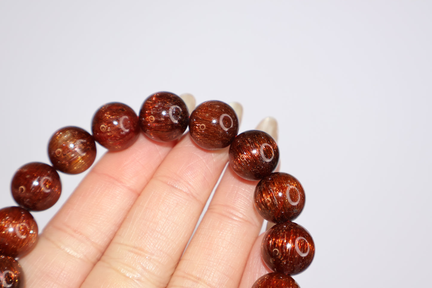 Detailed view of Red Rutilated Quartz beads held in hand, showcasing silky rutile threads and strong cat’s eye reflection, natural gemstone with deep reddish-brown tones.