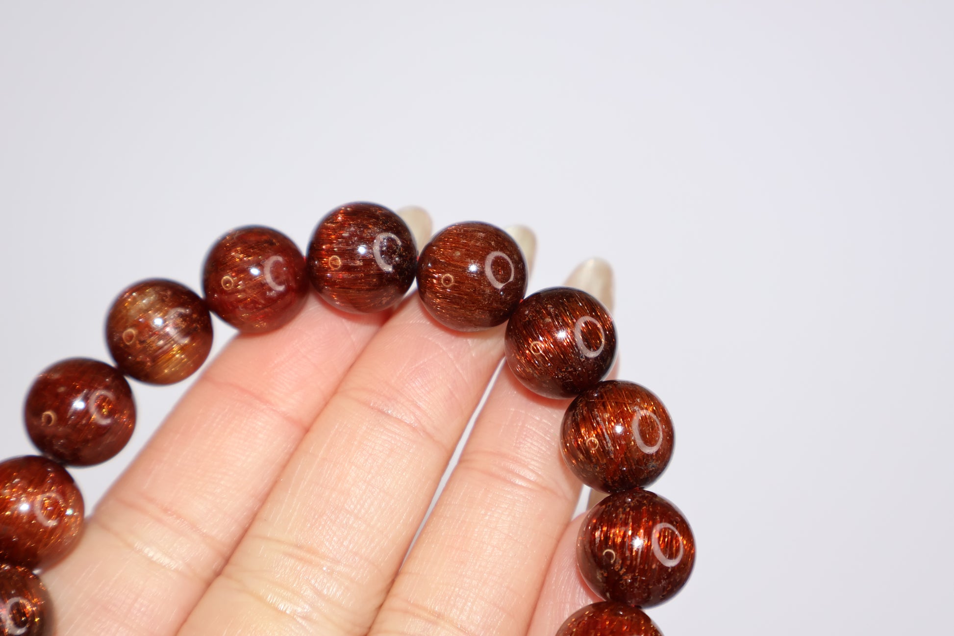 Detailed view of Red Rutilated Quartz beads held in hand, showcasing silky rutile threads and strong cat’s eye reflection, natural gemstone with deep reddish-brown tones.