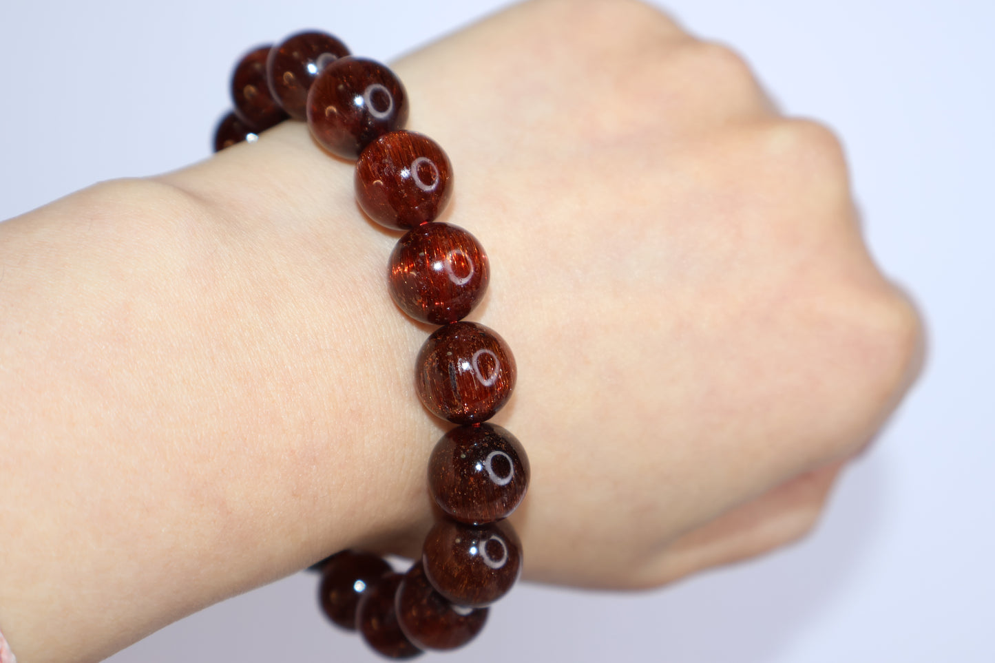 Red Rutilated Quartz bracelet worn on wrist, showing natural deep reddish tones and fine rutile threads, elegant gemstone jewelry with energetic cat’s eye shimmer.
