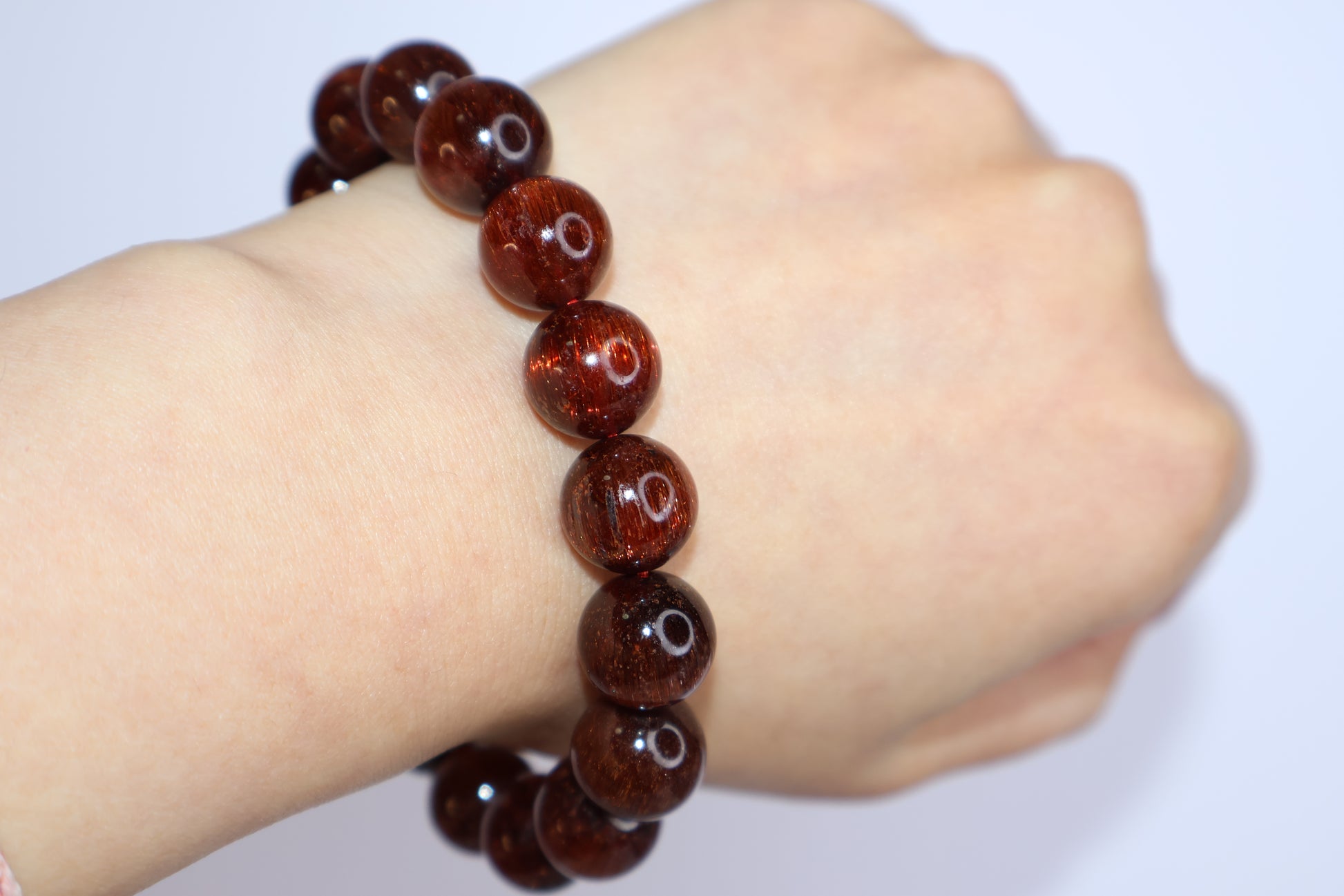 Red Rutilated Quartz bracelet worn on wrist, showing natural deep reddish tones and fine rutile threads, elegant gemstone jewelry with energetic cat’s eye shimmer.