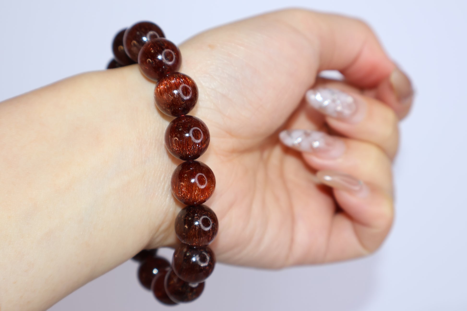 Red Rutilated Quartz bracelet worn on wrist with hand slightly clenched, highlighting the deep red hue, cat’s eye glow, and radiant rutile inclusions of the crystal beads.