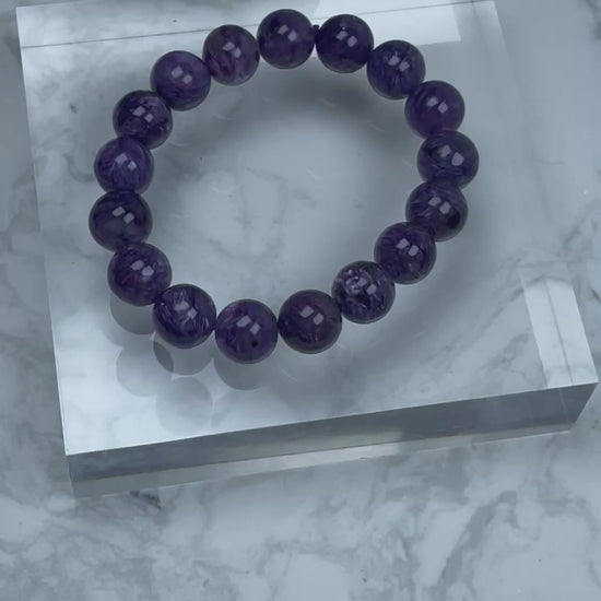 360-degree video showcasing a 12mm Charoite bracelet with deep purple hues and silky swirling patterns, highlighting the natural shine and fibrous inclusions of each bead.